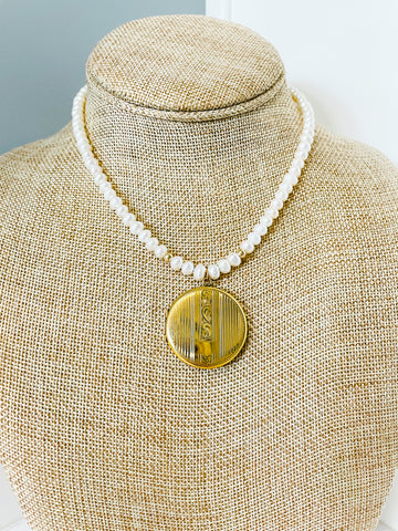 vintage gold embossed locket hangs from a freshwater pearl necklace